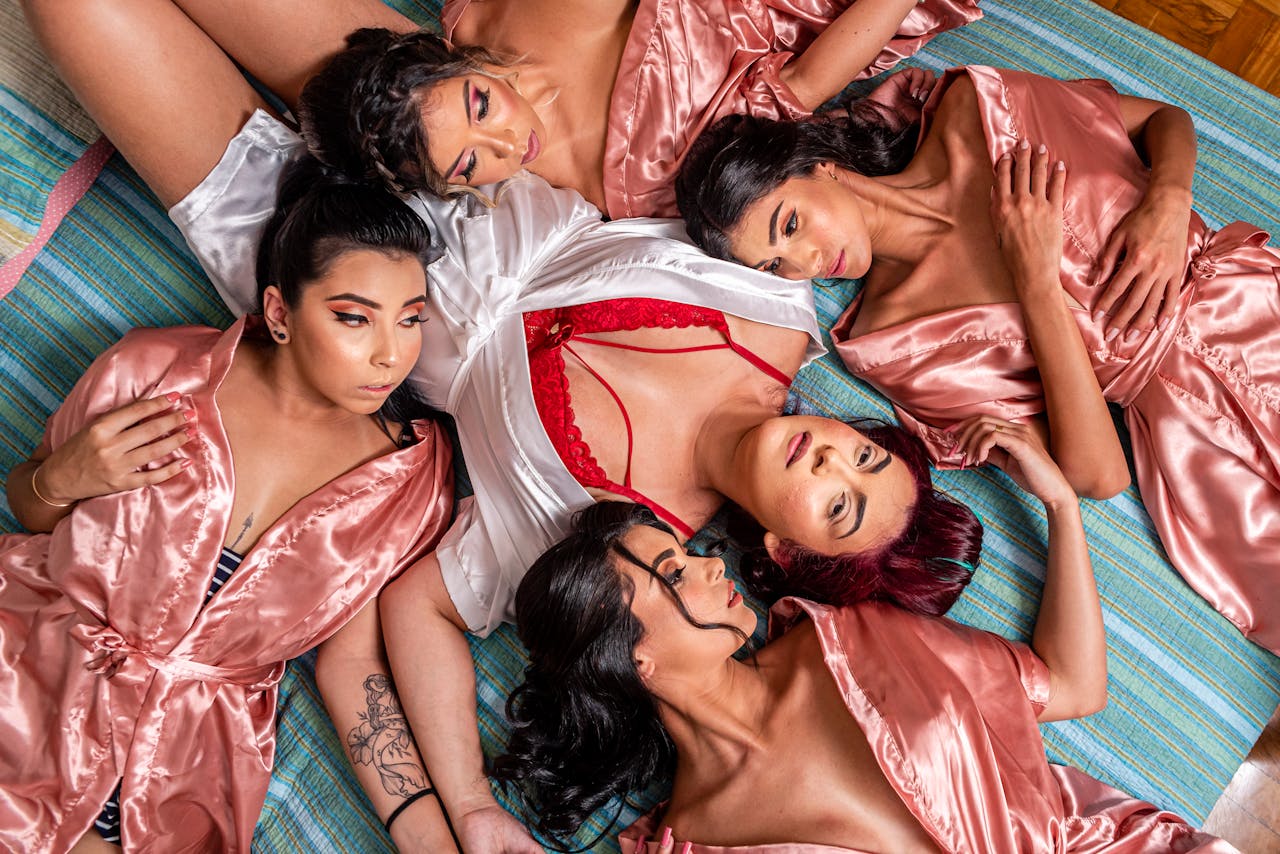 pexels-photo-10541681 Five women in satin robes lounging on a striped floor in an intimate setting, top view.