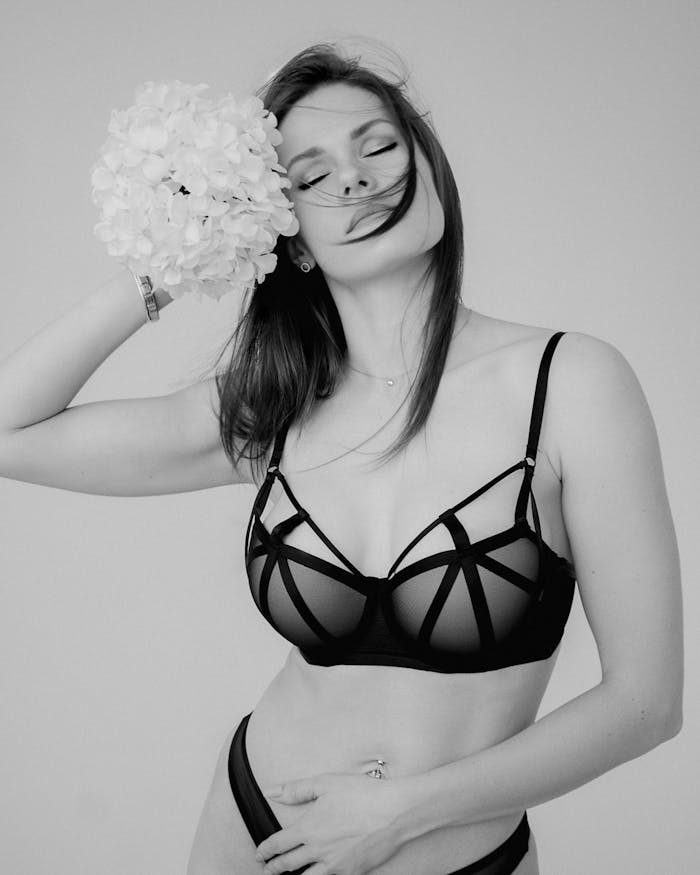 pexels-photo-19068711 Black and white portrait of a woman in lingerie holding flowers, eyes closed.